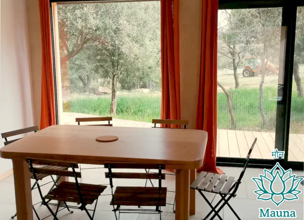 gîte à la ferme : salle à manger, baies vitrées, terrasse en bois et vue sur la cour-avant